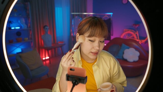 Girl beauty blogger in casual clothing shows a cosmetic powder in front of the camera at home studio.