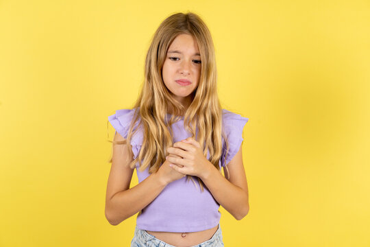 Sad blonde kid girl wearing violet T-shirt over yellow studio background desperate and depressed with tears on her eyes suffering pain and depression in sadness facial expression and emotion concept