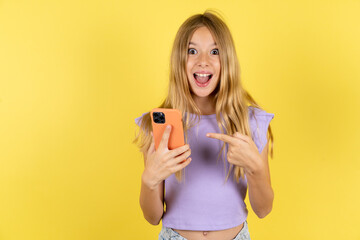 blonde kid girl wearing violet T-shirt over yellow studio background holding in hands showing new cell,