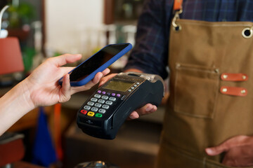 Close-up customer hand is using smartphone to scan QR code from credit card reader to pay for...