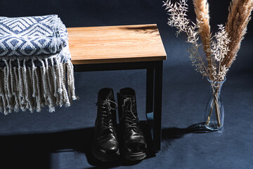 interior and home decor concept - close up of blanket on bench, lace-up boots and dry plants in vase in dark room