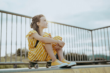 Mädchen, 9 Jahre, im gelbweiß gestreiften Jumpsuit mit Skateboard auf einer gelben Skaterbahn