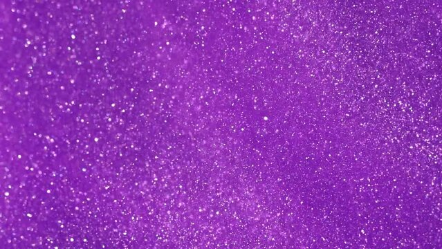 Slow Motion of silvery dust particles falling in purple fluid. Particles dispersion in colored liquid. Abstract gloating glitters background.