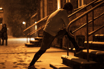 Young man stretching before jogging and exercising in the snow in the city during winter