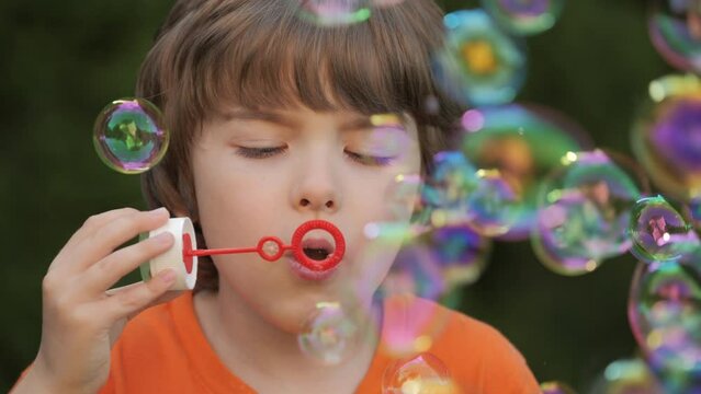 Little Boy Blowing Soap Bubbles Having Fun Playing Outside, Child Innocence and Curiosity. Boy Kid Blowing Soap Bubbles in Park, Garden and Nature, Having Fun, Joy and Childhood Development, Freedom.
