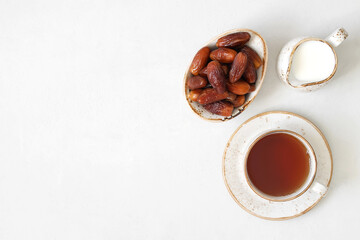 A cup of tea, dried dates and milk jug on a white background. Natural healthy breakfast. Copy space, top view, flat lay.