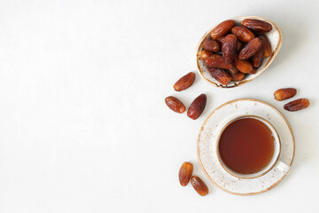 Dried dates in a bowl and a tea drink on white background with copy space. Traditional Arabic sweets. Popular food for Ramadan. Top view, flat lay.