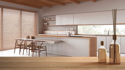 Wooden table top or shelf with aromatic sticks bottles over minimal japandi white kitchen with island, modern architecture interior design