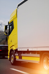 Side view of the long range truck on the European highway. Express delivery and shipping of the goods. Door to door logistics. Semi truck with a yellow cabin and white trailer. Customers support