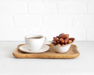 Dried dates in a bowl and a tea drink in wooden tray on a white background. Popular food for Ramadan. Oriental sweets.