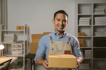 Asian male small business owner using mobile app on smartphone checking parcel box. Warehouse worker, seller holding phone scanning retail dropshipping package postal parcel bar code.