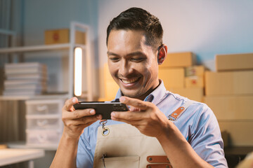 Asian male small business owner using mobile app on smartphone checking parcel box. Warehouse...