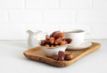 Dried dates in a bowl closeup on white background. Dates, tea and milk jug in a wooden tray. Traditional Arabic food.