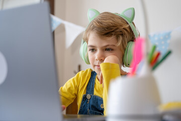 Fototapeta premium Primary school Student child with headphones video call with teacher using laptop.