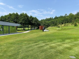 Fototapeta na wymiar Glass modern golf club building and white golf balls lie in basket on green grass on sunny summer day. A place to play golf