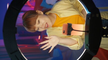 Appealing girl vlogger in casual clothing doing a live broadcast on her smartphone. Vertical photo