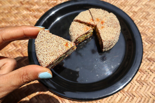 Female holding Slices of Anjeer cake, Indian sweet dish item covered with poppy seeds. Fig dessert with filling of dates, cashewnuts almonds and pista