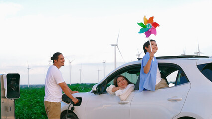 Concept of progressive happy family enjoying their time at wind farm with electric vehicle....