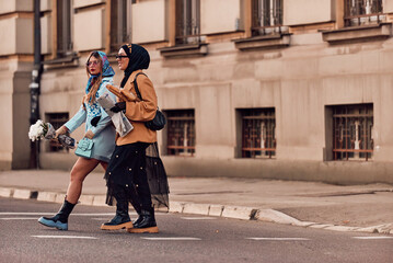 Couple woman one wearing a hijab and a modern yet traditional dress, and the other in a blue dress...