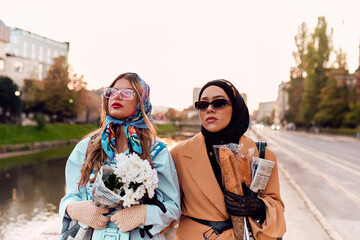 Couple woman one wearing a hijab and a modern yet traditional dress, and the other in a blue dress...