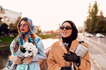 Couple woman one wearing a hijab and a modern yet traditional dress, and the other in a blue dress...