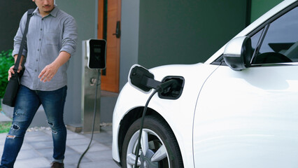 A man unplugs the electric vehicle's charger at his residence. Concept of the use of electric...