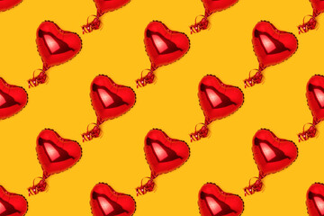 Repetitive pattern made of red inflatable foil balloons in a heart shape. Creative concept on a yellow background.