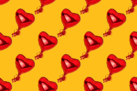 Repetitive pattern made of red inflatable foil balloons in a heart shape. Creative concept on a yellow background.