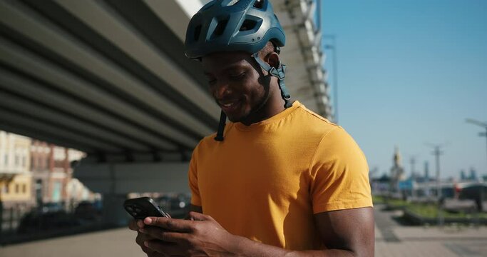 African American guy in helmet types message on smartphone
