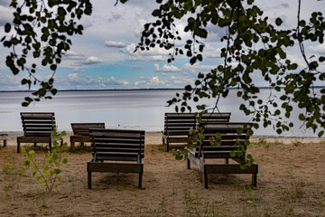 Fototapeta premium Sun loungers on the bank of a wide river. Blue sky, sand. Summer day