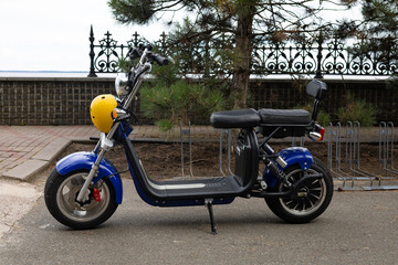 A beautiful electric moped with a helmet is parked on an asphalt road in a park