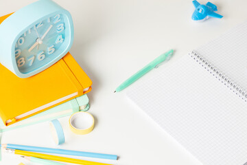 Back to school background. School accessories, notebook, pens, alarm clock on white wall background. Education, studing and back to school concept. 