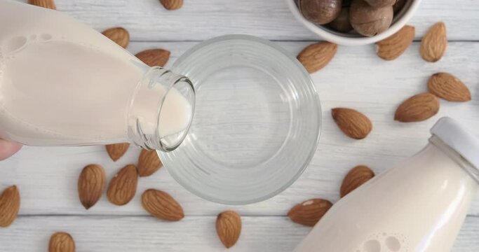 Alternative milk, pouring almond milk into a glass placed on table from bottle, vegan drink made of almond nuts, slow motion video clip, non-dairy product, top table view, horizontal 4k footage