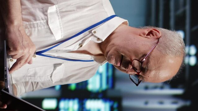 Vertical video Focused IT support executive in data storage company equipped to handle complex computational operations, doing checking on server devices, verifying efficiency parameters to prevent