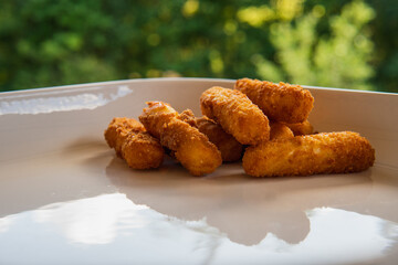 Delicious golden deep fried halloumi sticks, cheese, on a white plate. Natural lighting in the summertime. Garden in the background.