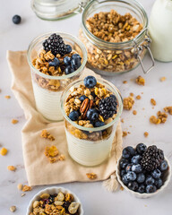 Two glasses with Greek yogurt, granola, blueberries and blackberries, bowls of muesli.
