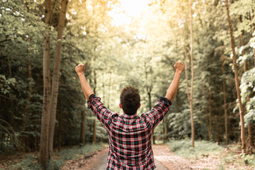 Fototapeta na wymiar Happy strong young man with raised arm raised in autumn forest surrounded by beautiful nature