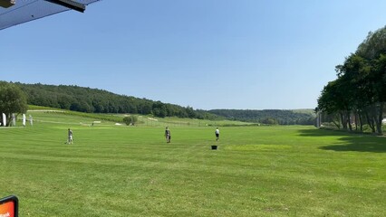 Three employees of the golf club clean the green lawn after the game with special equipment and collect balls on the field in a basket. Golf course attendants