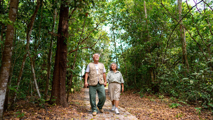 Naklejka na ściany i meble Asian senior couple relax and enjoy outdoor lifestyle travel nature hiking together at tropical forest trail on summer vacation. Retired elderly people leisure activity and mental health care concept.