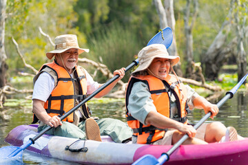 Asian senior couple kayaking together in the lake at mangrove forest on summer vacation. Retired elderly people man and woman have fun outdoor lifestyle travel nature and rowing a boat in the river.