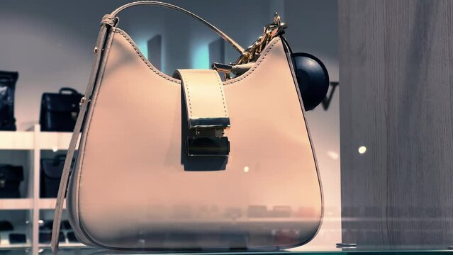 Women's beige leather handbag on a glass shelf in an accessories store