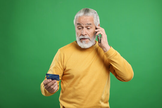 Confused Senior Man With Credit Card Talking On Smartphone Against Green Background. Be Careful - Fraud