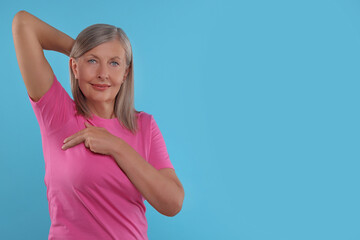 Beautiful senior woman doing breast self-examination on light blue background, space for text