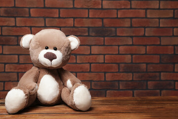 Cute teddy bear on wooden table near brick wall, space for text