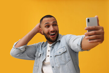 Smiling young man taking selfie with smartphone on yellow background