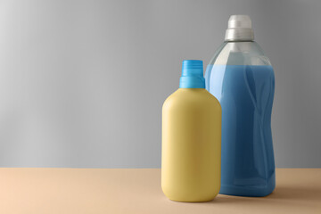 Bottles of fabric softener on pale yellow table against light grey background, space for text
