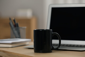 Black ceramic mug and laptop on wooden table at workplace