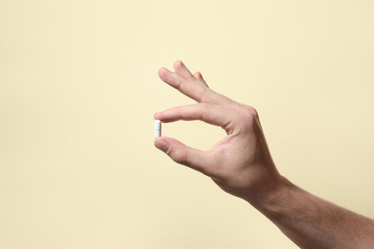 Man holding pill on beige background, closeup