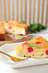 Piece of delicious pineapple pie with cherry and mint on white table