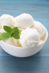 Delicious vanilla ice cream and mint in bowl on light blue wooden table, closeup